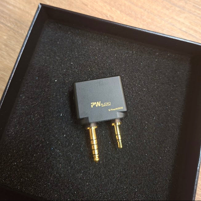 Black audio adapter with gold connectors on a black box lid